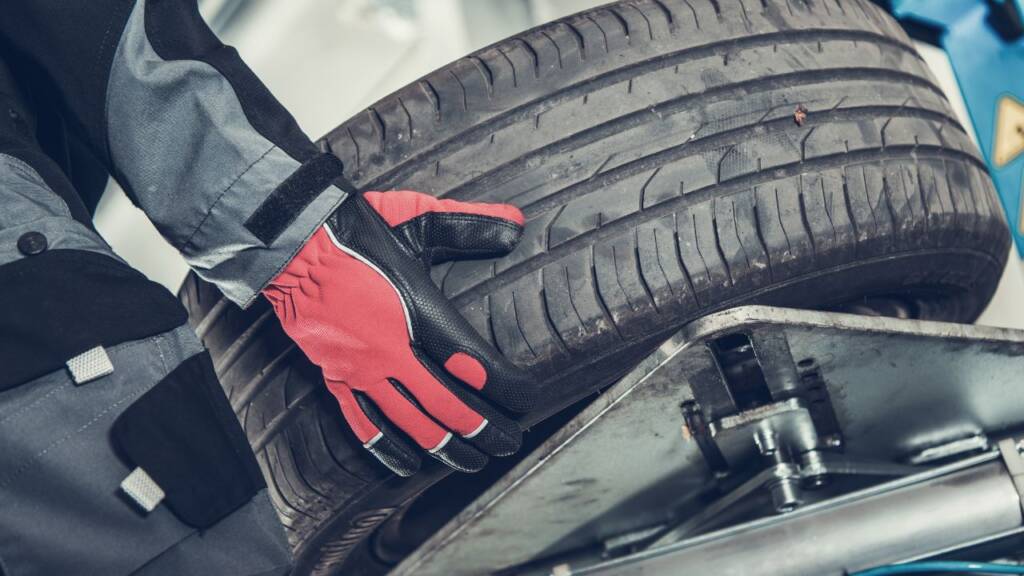 Obrazek przedstawia mechanika, który wymienia oponę