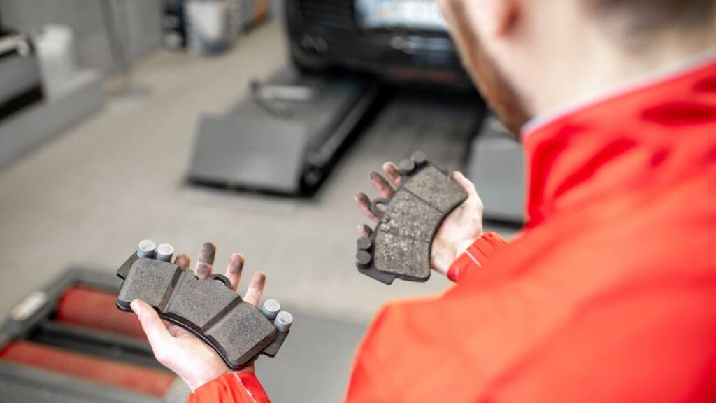 Obrazek przedstawia mechanika, który trzyma klocki hamulcowe