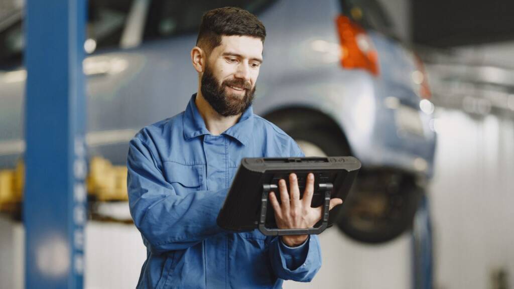 Obrazek przedstawia mechanika, który sprawdza coś na tablecie