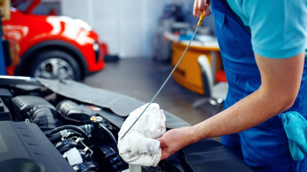 Obrazek przedstawia mechanika, który sprawdza stan oleju silnikowego